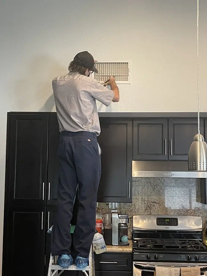 Technician inspecting an air vent during HVAC service in Triangle
